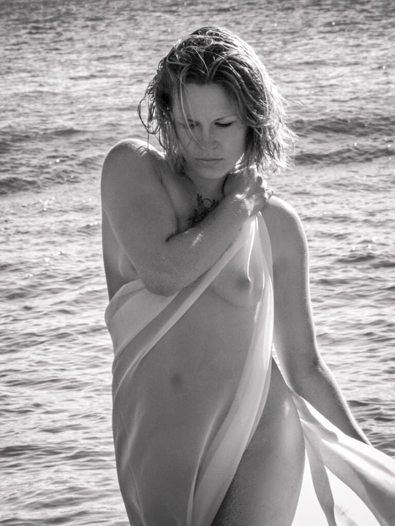 Fine art nude with sheer fabric standing by the ocean in black and white