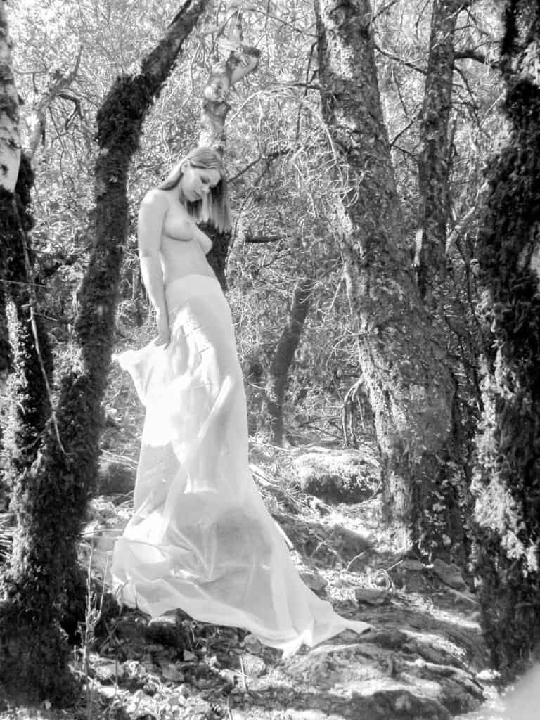 Fine art nude standing in forest with translucent fabric in black and white