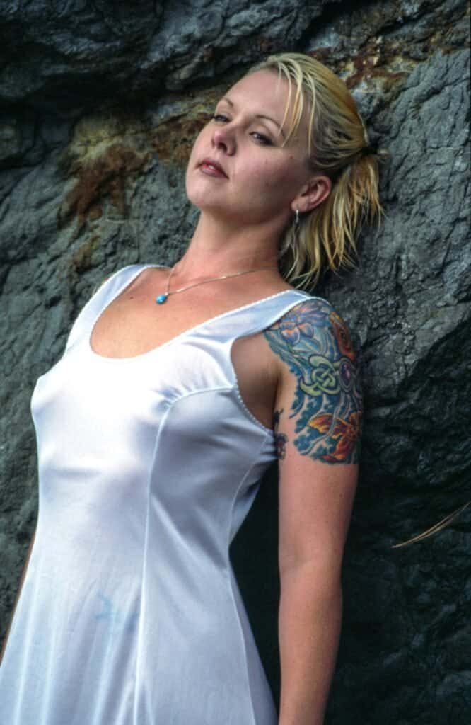 Outdoor portrait of a blonde woman with a colorful arm tattoo leaning on rocks
